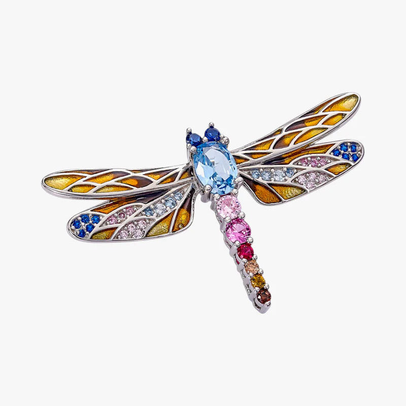A dragonfly-shaped brooch featuring a silver-toned metal body and wings, embellished with yellow, blue, pink, and orange gemstones on a light gray background.