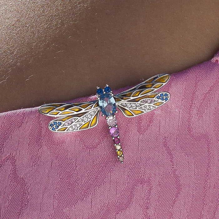 A close-up of a dragonfly-shaped brooch pinned to a pink textured fabric against a person's skin.