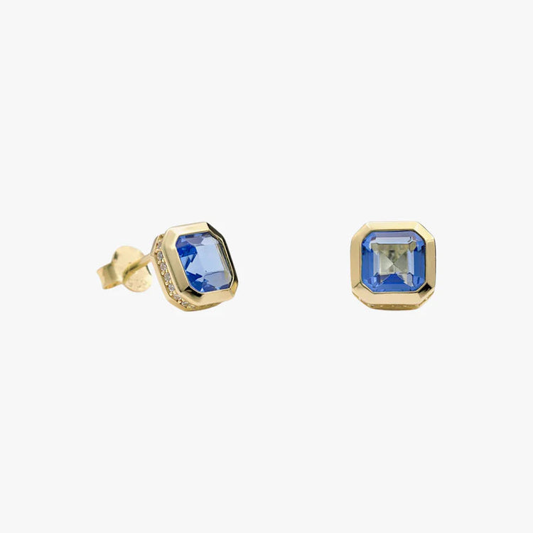 A pair of gold stud earrings featuring square blue gemstones with a faceted gold border, shown on a plain light gray background.