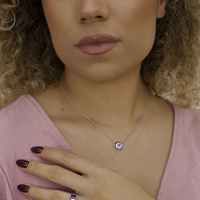A close-up lifestyle shot of a woman wearing a silver ring with a purple crystal cluster and a delicate silver necklace with a matching circular pendant, styled with a pink top.