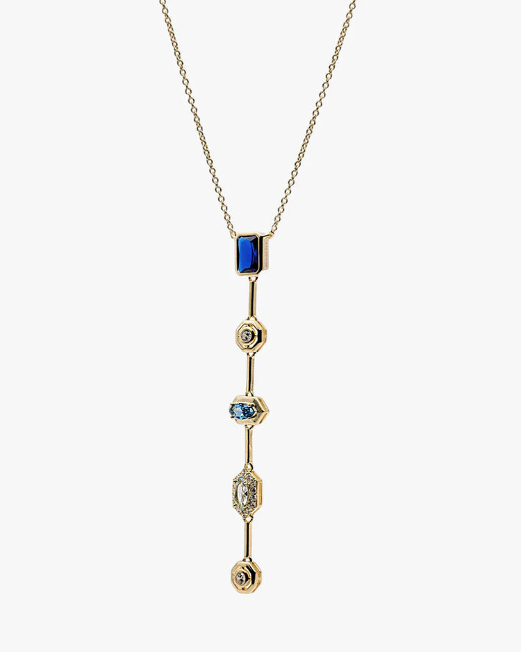 A gold chain necklace with a long, vertical drop pendant featuring a rectangular blue stone at the top and three smaller blue and clear gemstone accents on a light gray background.