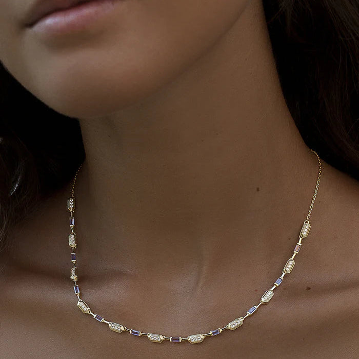 A delicate gold necklace with small faceted beads, worn on a model's neck. 