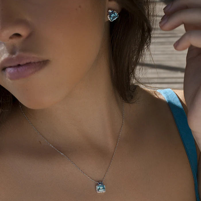 A close-up lifestyle shot of a model wearing a silver pendant necklace and matching stud earring.