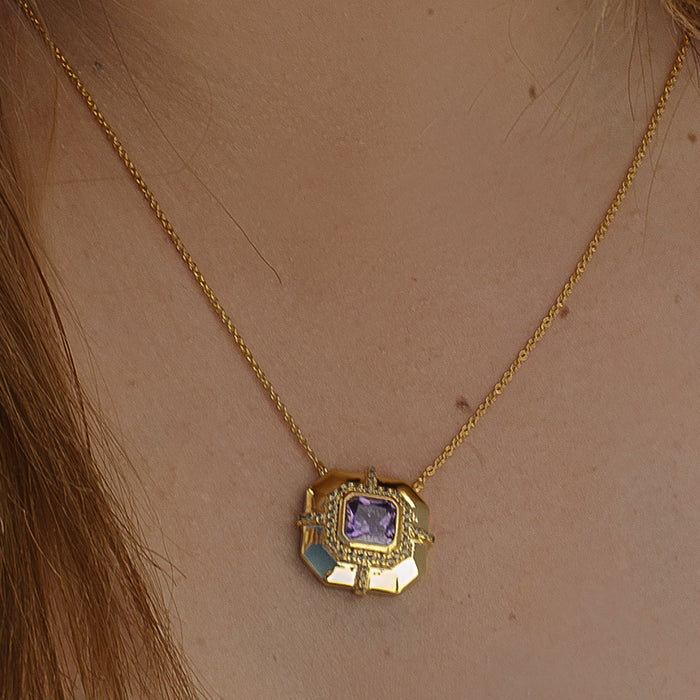 A gold chain necklace with a geometric pendant featuring a purple square gemstone and light blue accents, worn on a person's neck.
