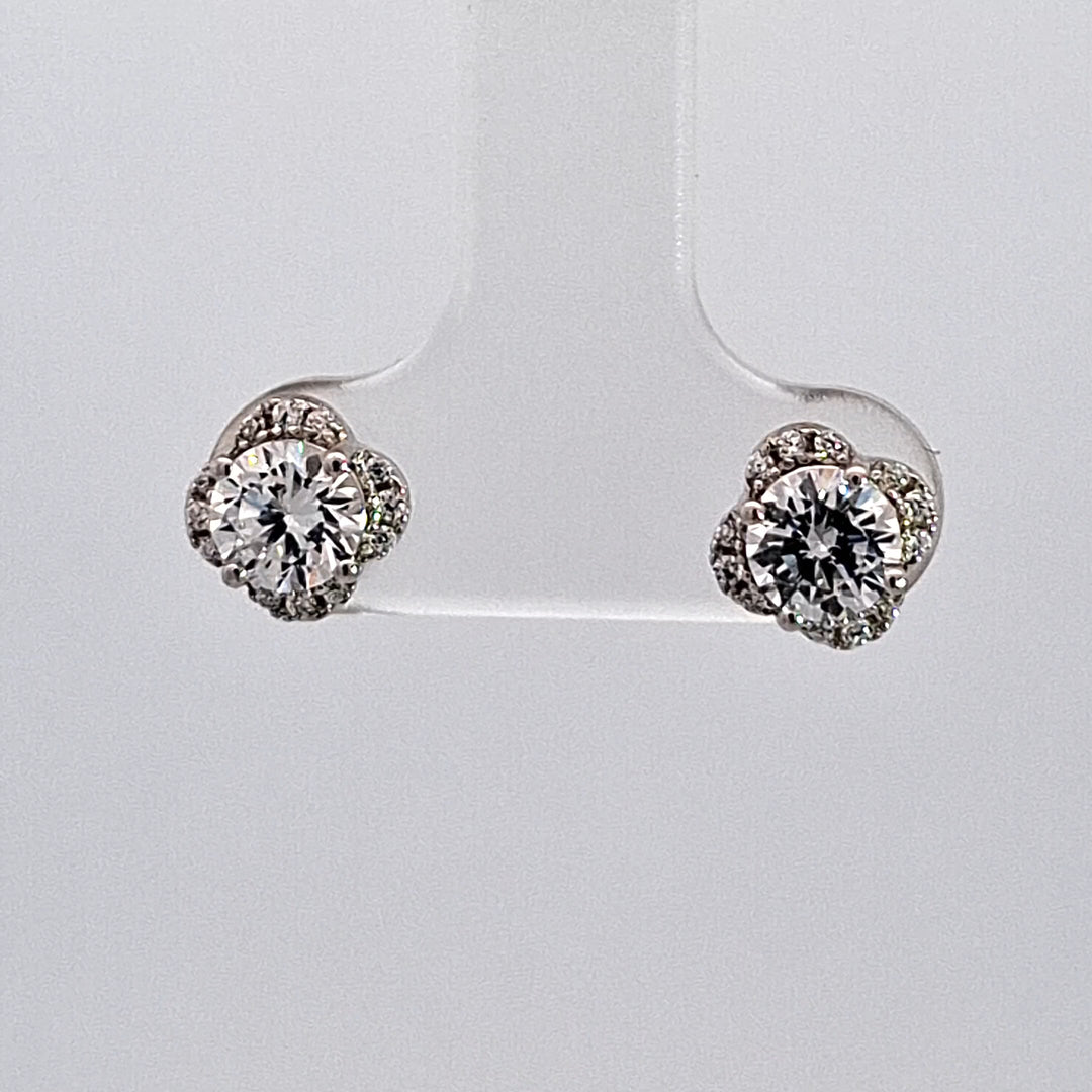 Pair of diamond earrings on a clear stand against a light gray background