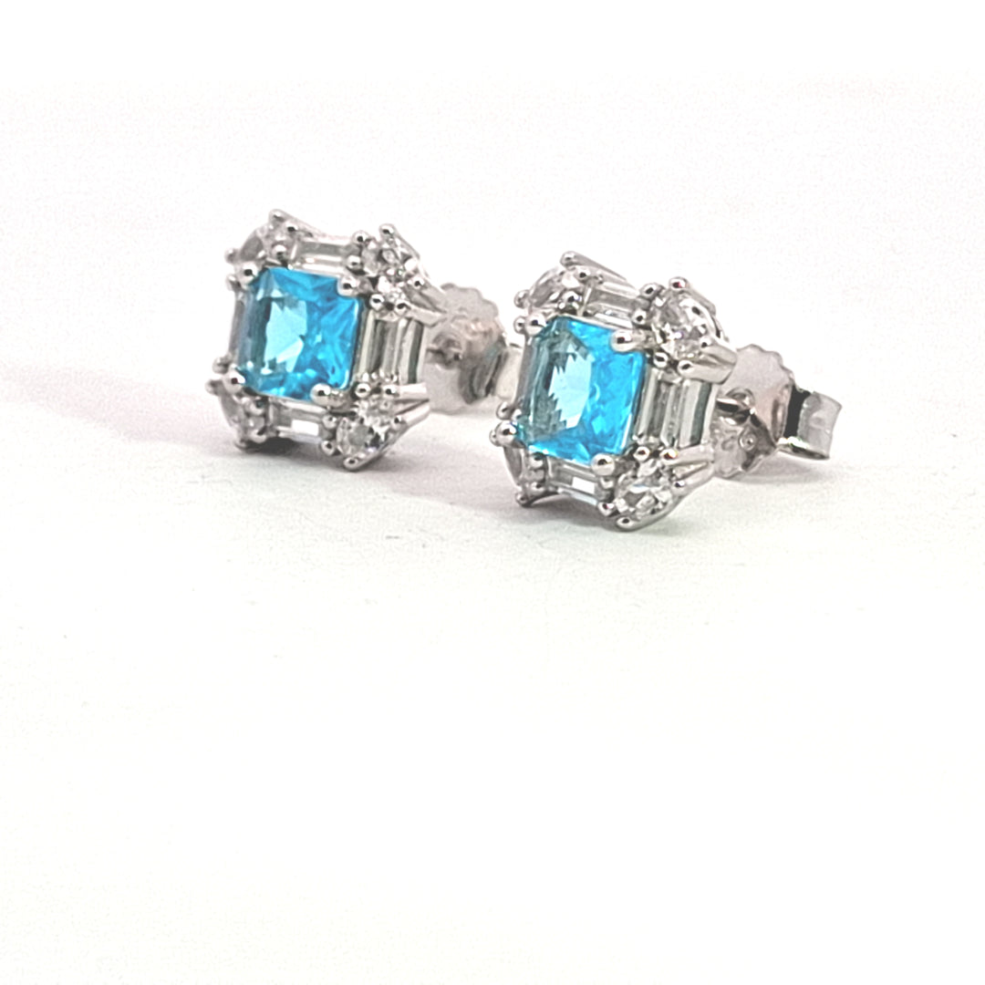 A pair of sterling silver square shape stud earrings set with aqua blue CZs surrounded by baguettes and round CZs at the corners.
