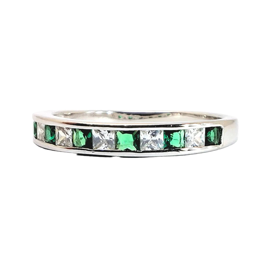 A silver band ring featuring a channel setting of alternating square-cut green emeralds and clear stones, shown against a plain white background.