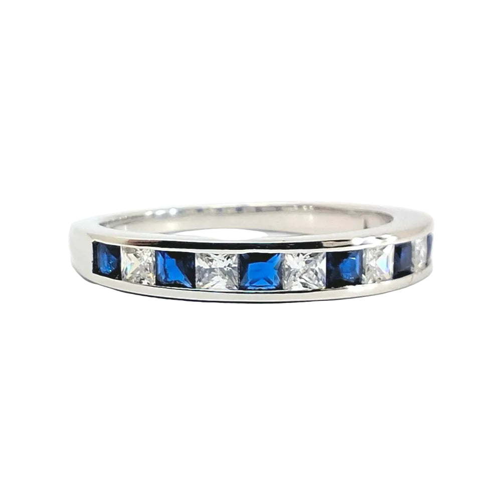 A silver band ring featuring a row of alternating square-cut blue and clear stones, photographed on a plain white background.